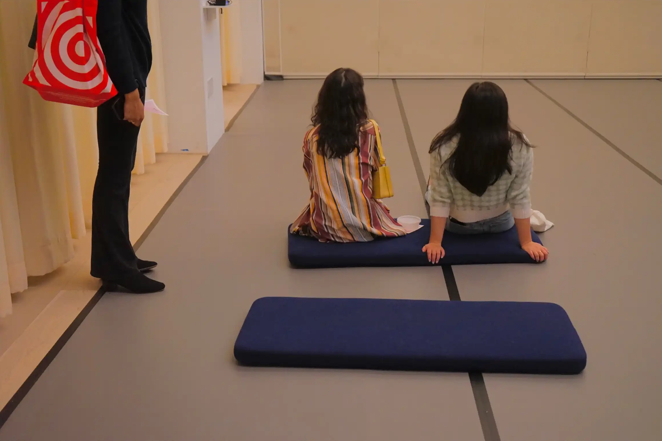 Two attendees sit on yoga mats and conversate, away from the dining table