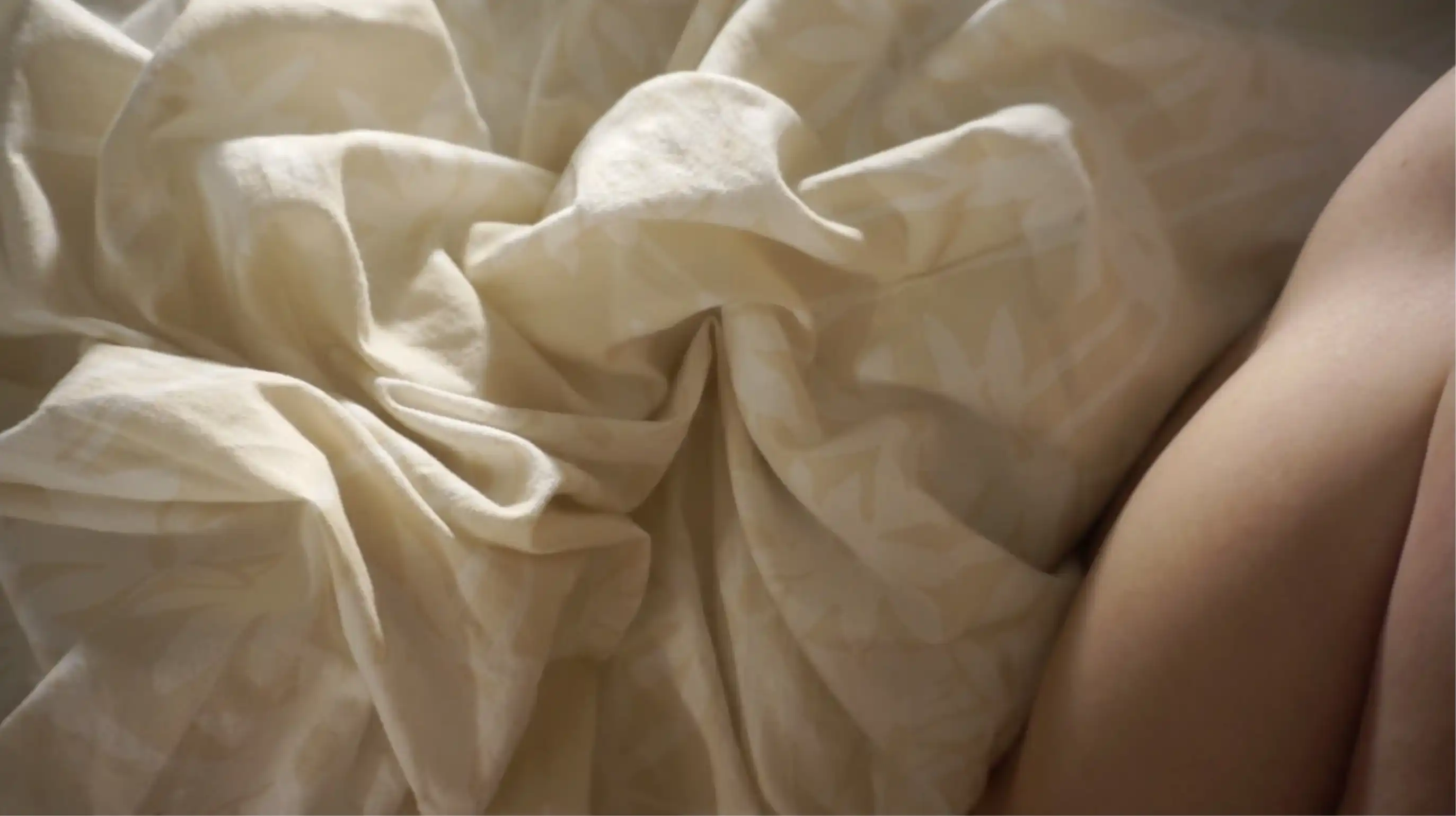 An unintelligible body part over wrinkled bedding