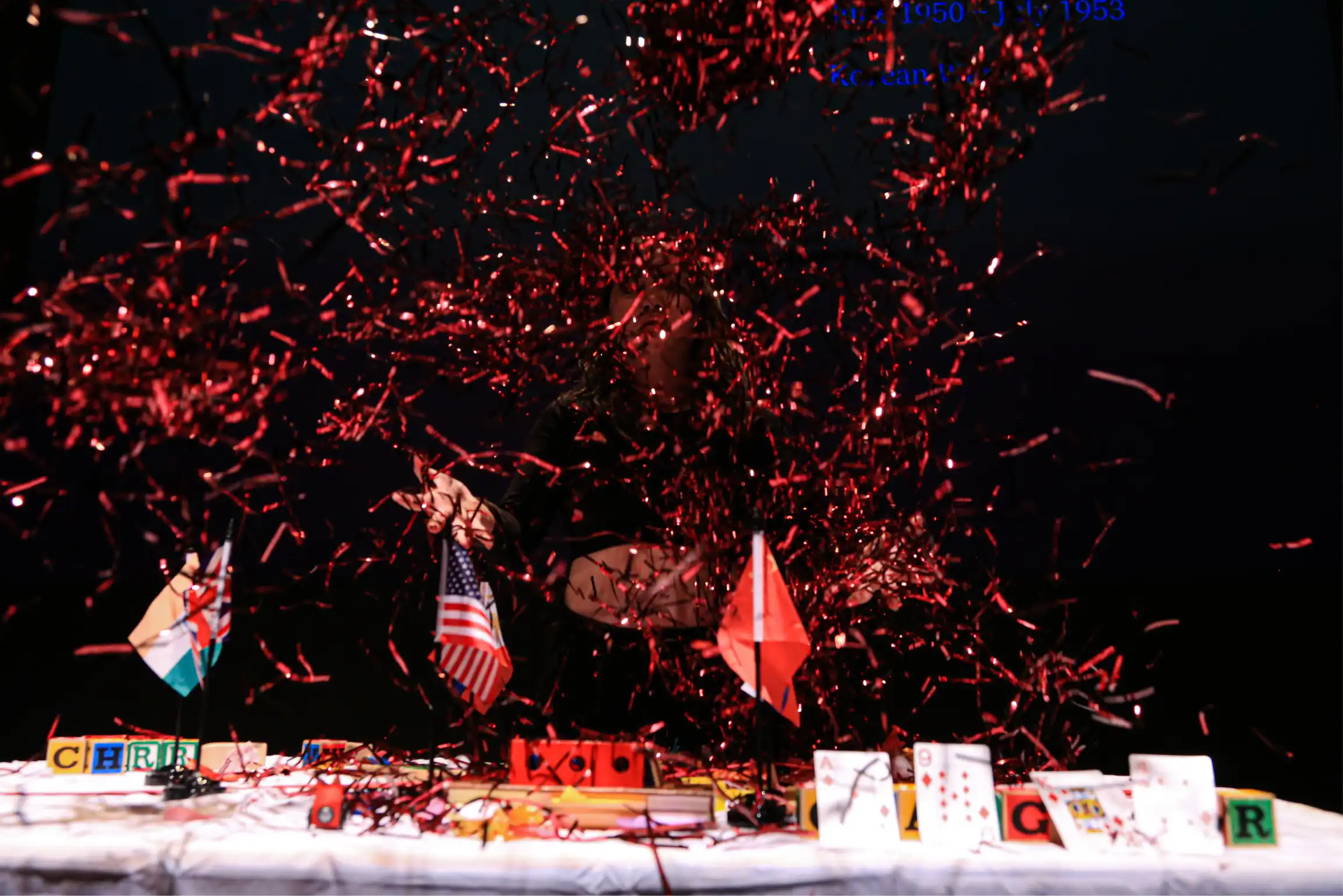 Confetti fall over a plastic table with American and Russian miniature flags, playing cards, wood blocks, and other toys